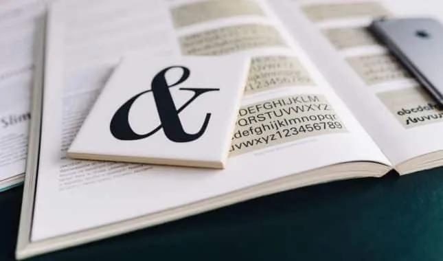 Aufgeschlagenes Schriftmusterbuch mit Alphabeten, darauf eine Karte mit grossem Ampersand.