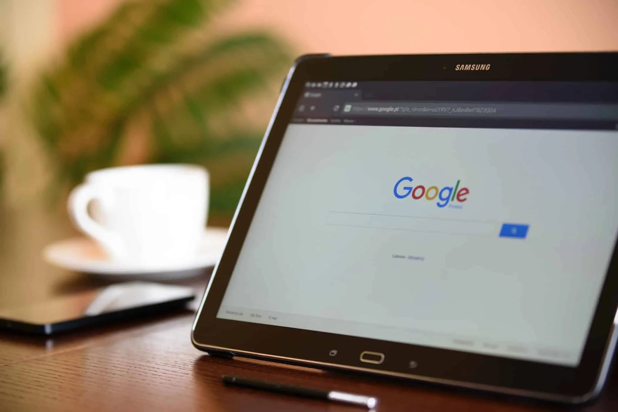 Tablet auf einem Holztisch mit geöffneter Google-Suche, daneben Kaffeetasse und Stift.