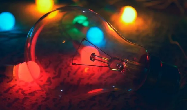 Klare Glühbirne liegt vor bunten Lichterketten, die sie rot, blau und grün anleuchten