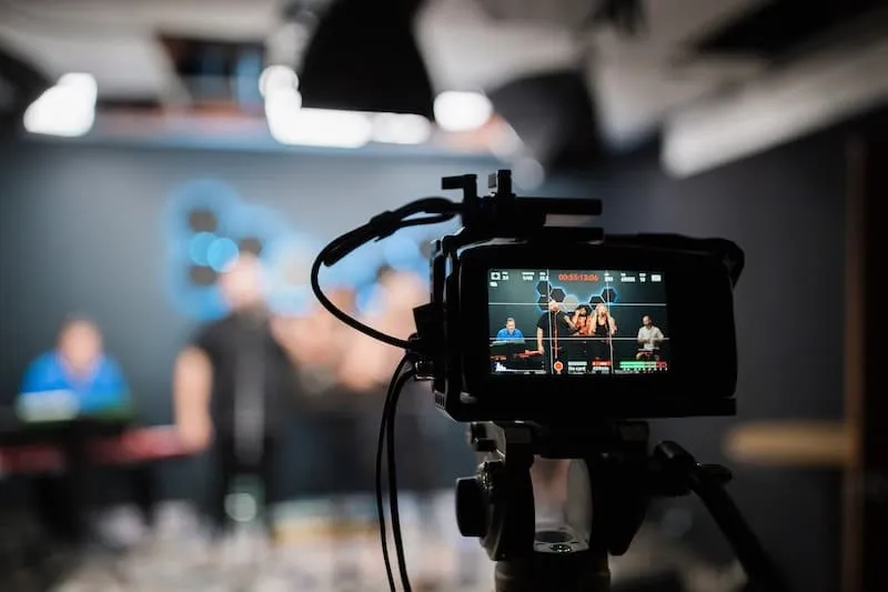 Kamera auf Stativ im Studio, ihr Display zeigt die laufende Aufnahme einer Band mit Timecode.