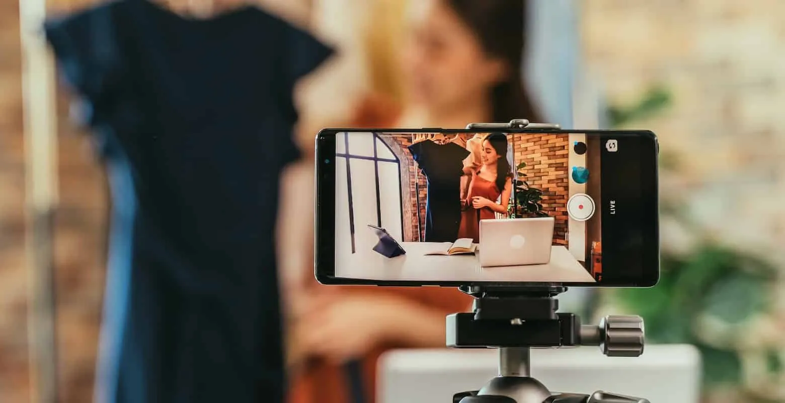 Smartphone auf Stativ filmt live: auf dem Display präsentiert eine Frau Kleider im Laden