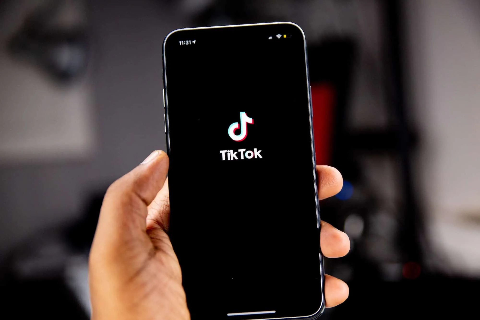 Hand hält ein Smartphone, auf dem der TikTok-Startbildschirm mit Logo zu sehen ist.