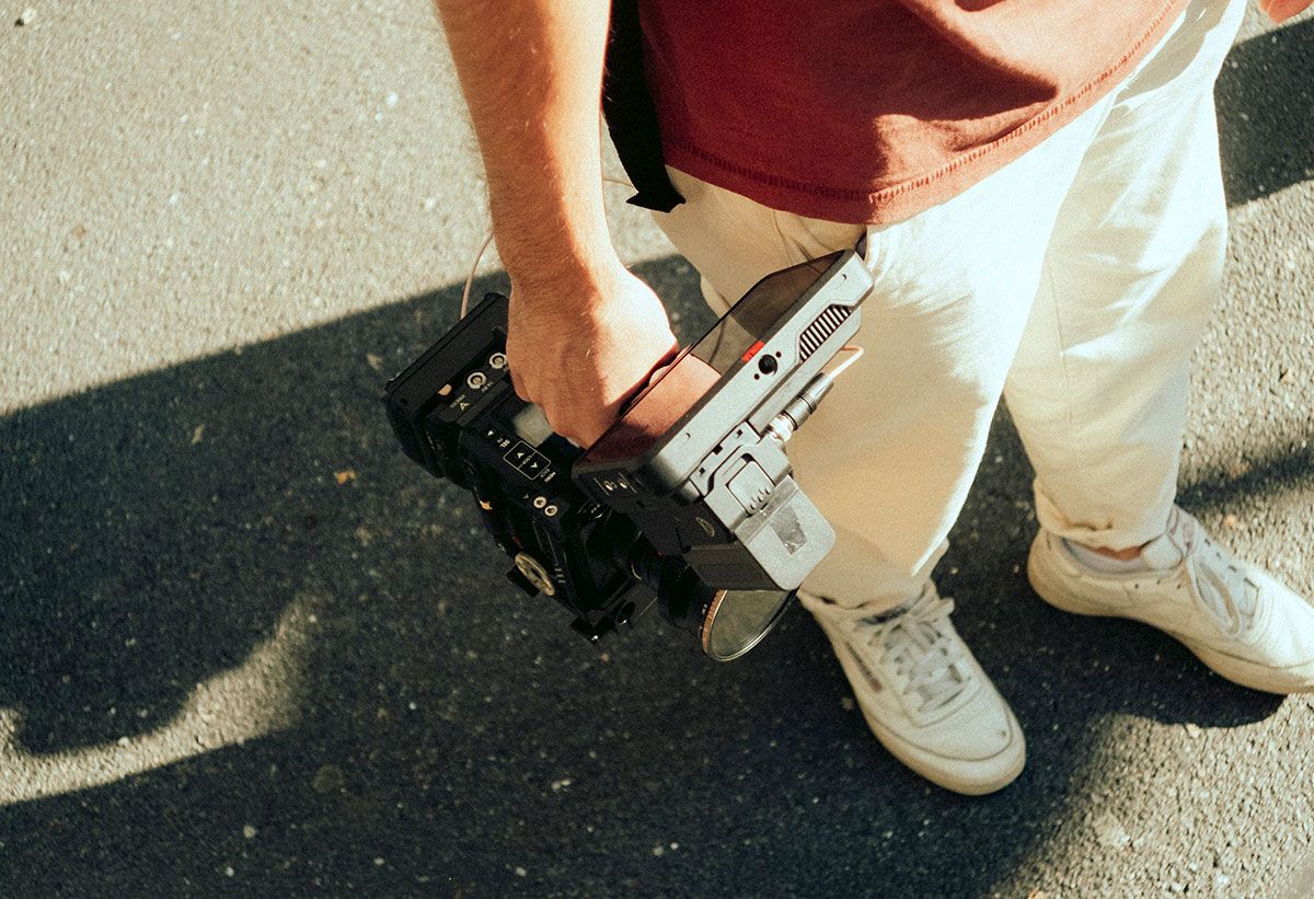 Eine Person trägt eine Filmkamera auf einer sonnigen Strasse.