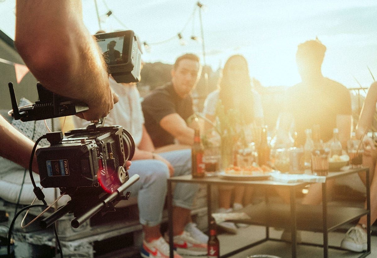 Eine Filmkamera nimmt eine Gruppe beim Apéro im Abendlicht auf.